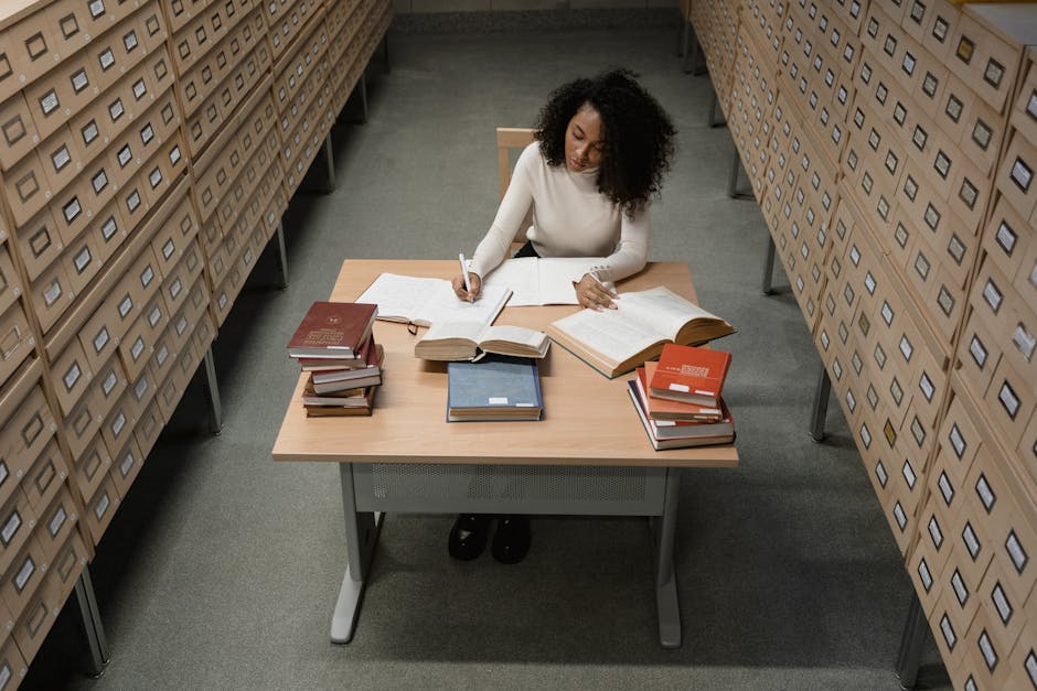 An African American woman studying at a wooden desk surrounded by drawers in an archive room.